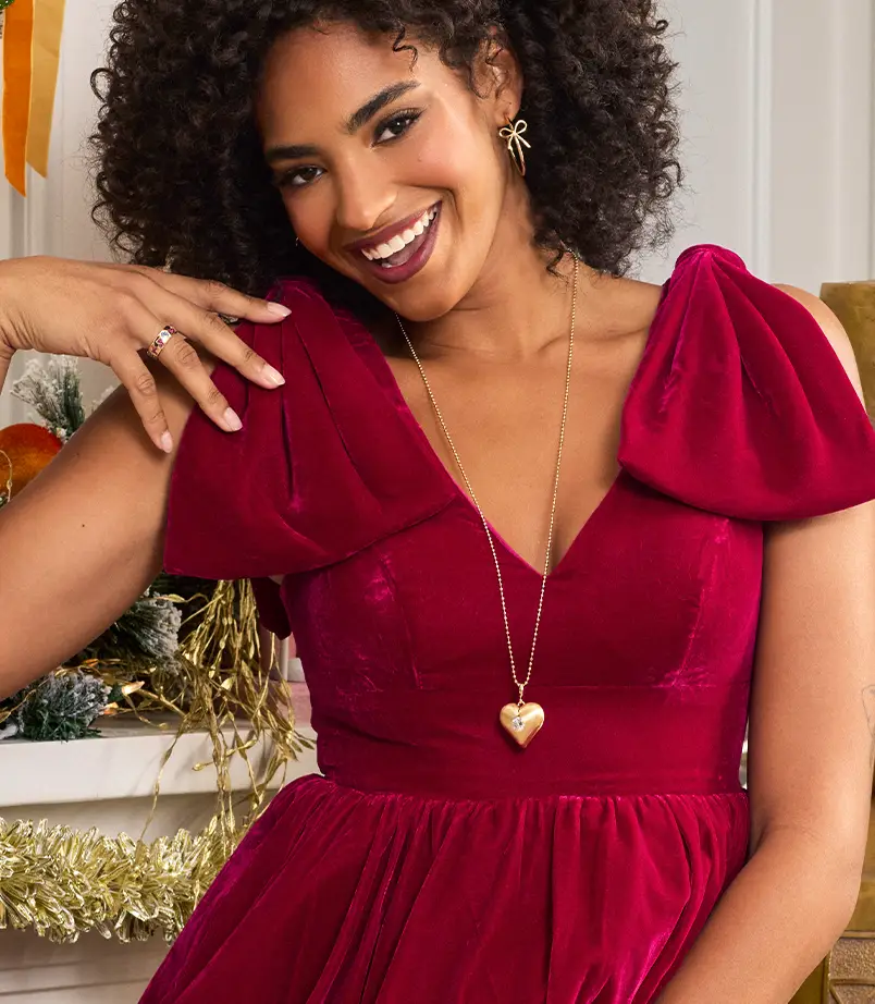 Model in a red dress wearing a gold necklace with heart pendant on it