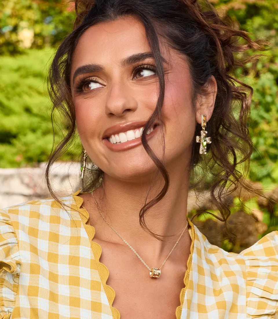Model in a green derss wearing gold gemmed neckles with larger hoop earrings